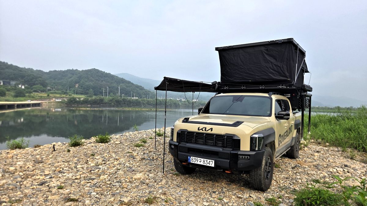 Kia Tasman by a river with the GOAT camper's roof up